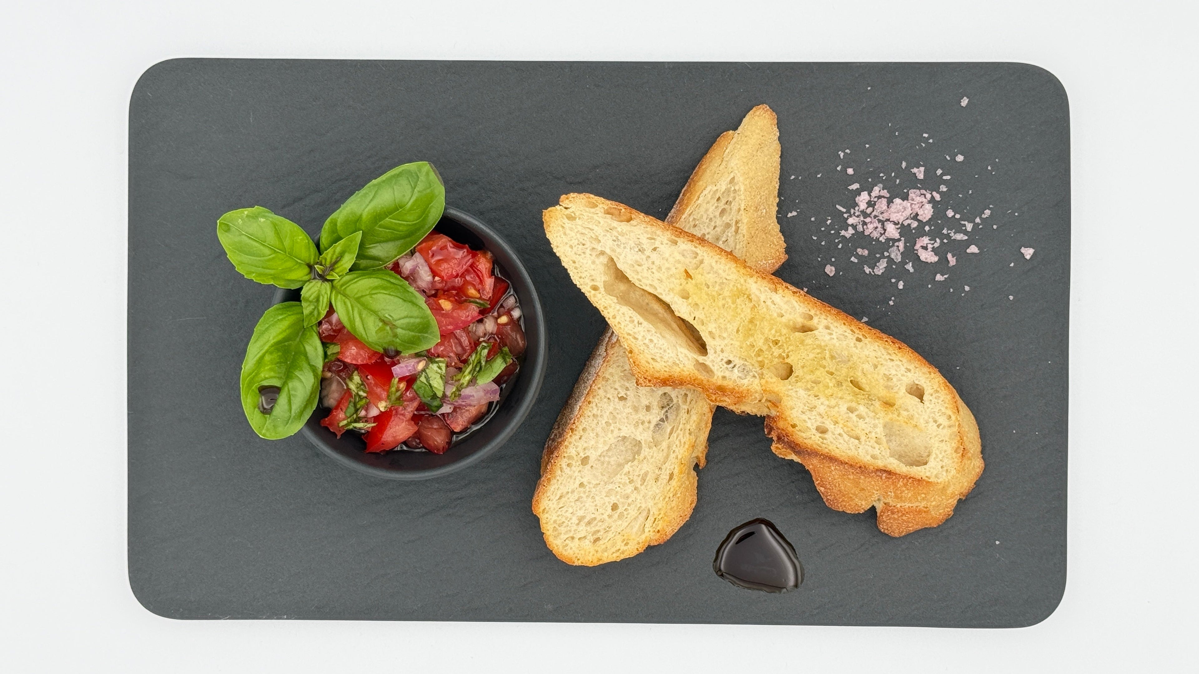 Bruschetta selbst-gemacht mit reifen Tomaten, Basilikum, roter Zwiebel, Olivenöl, Meersalz und Tellicherry Pfeffer auf geröstetem Brot