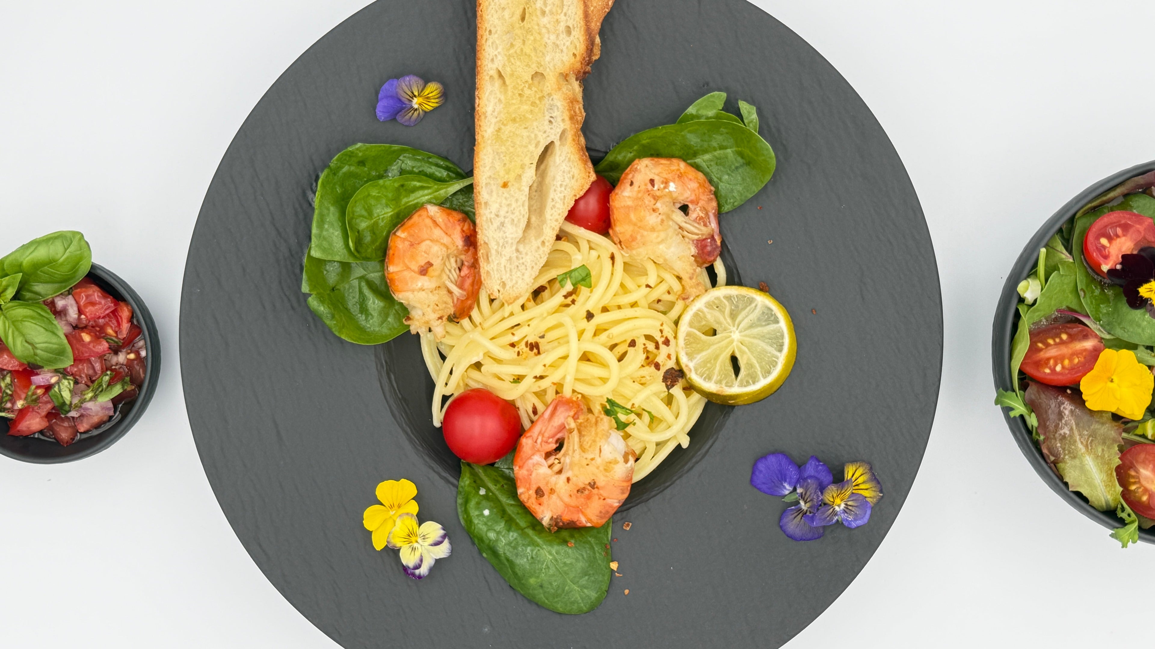 Cremige Zitronenpasta mit Parmesan, gebratenen Black Tiger Garnelen, frischem Spinat und gerösteter Zitronenzeste auf einem Teller angerichtet